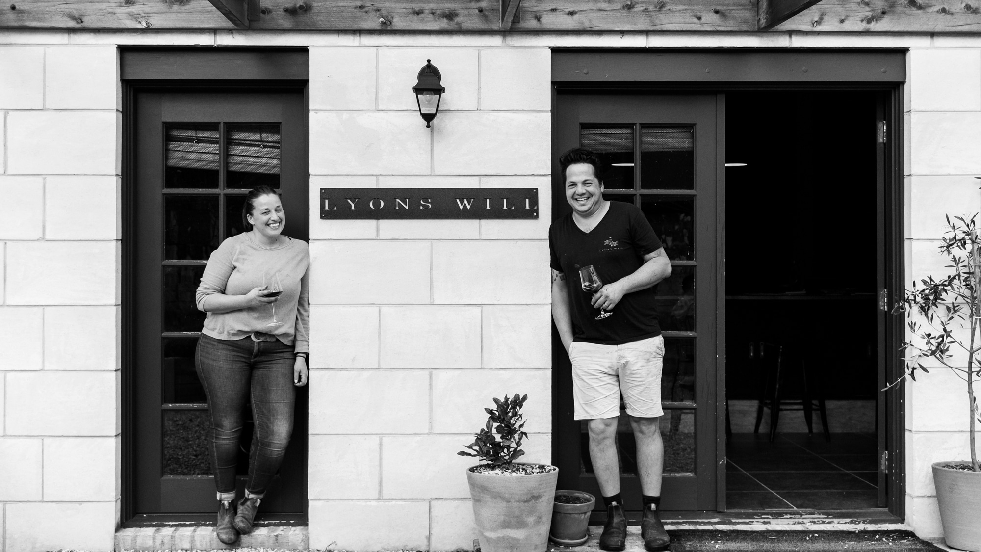 Man and woman in black white photo posing in front of winery door 